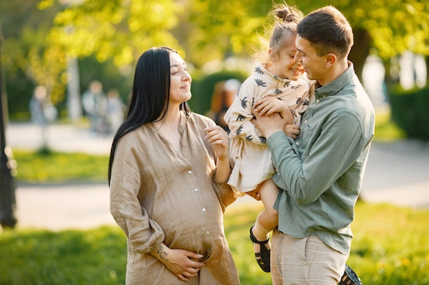 Mère enceinte et sa petite fille et son mari debout dans un parc et se serrant dans leurs bras