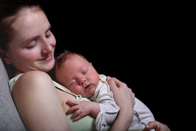 Mère endormie avec un bébé endormi sur la poitrine, un moment de tendresse. Noir, espace pour le texte