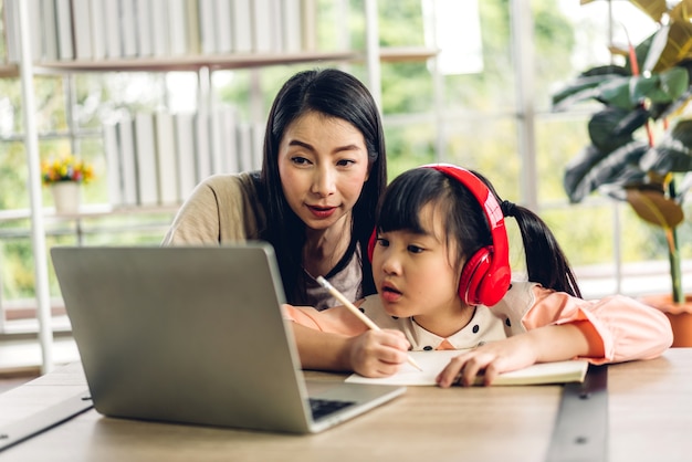 Mère et enfant asiatique petite fille apprenant et regardant un ordinateur portable à faire ses devoirs en étudiant les connaissances avec le système d'apprentissage en ligne de l'éducation en ligne