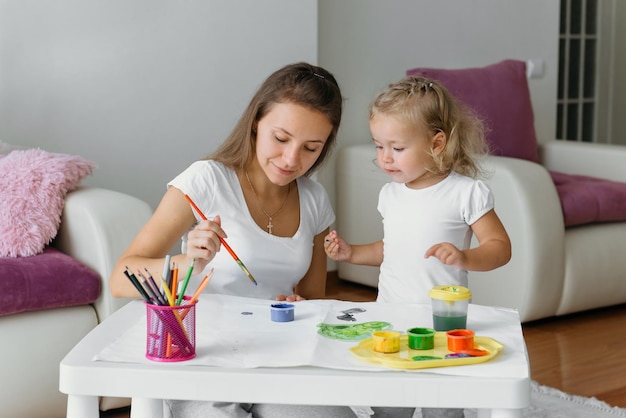 Mère et enfant en bas âge peignant à la maison la famille créative