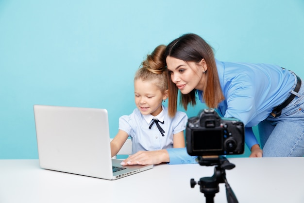 Mère avec enfant blogueur en face de la caméra d'enregistrement vidéo assis à la table dans le studio bleu.