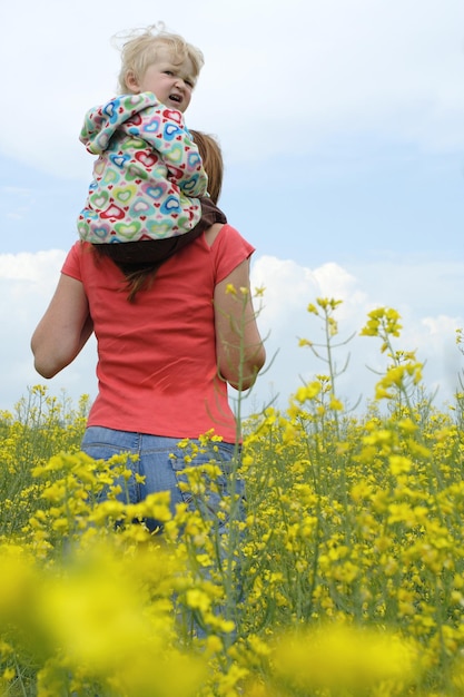 Mère avec enfant sur un champ jaune en fleur avec ciel bleu et nuages blancs