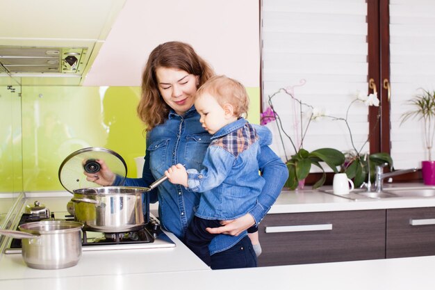 Mère et enfant dans ses bras préparant le dîner dans la cuisine. Mère et son petit garçon cuisinant la soupe ensemble