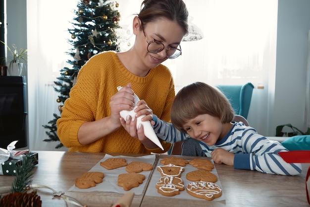 Mère et enfant décorant des biscuits de pain d'épice de Noël avec du glaçage au sucre et s'amusant ensemble