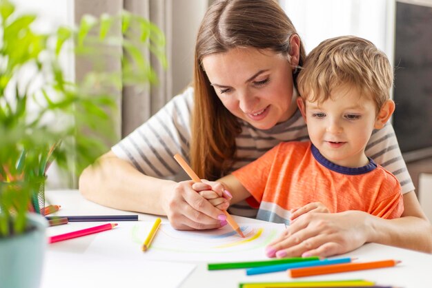 Mère et enfant dessinant avec des crayons assis au bureau à la maison