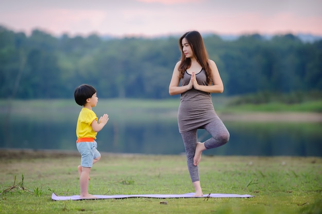 Mère et enfant faisant des exercices de yoga sur l'herbe au parc avant le coucher du soleil en été.