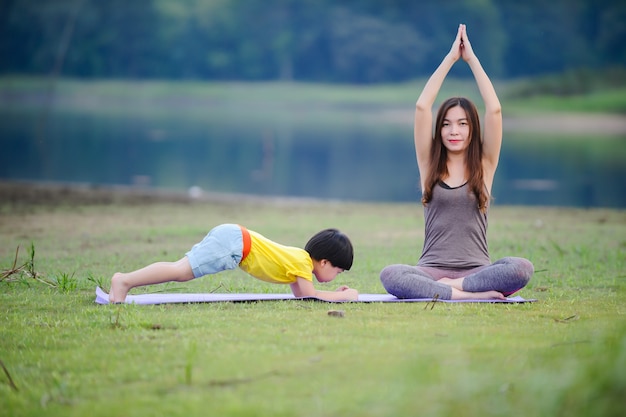 Mère et enfant faisant des exercices de yoga sur l'herbe au parc avant le coucher du soleil en été.