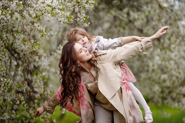 Mère avec enfant fille jouant dans le jardin de printemps fleuri. Femme avec sa fille étreindre et s'amuser à l'extérieur. Concept de famille heureuse