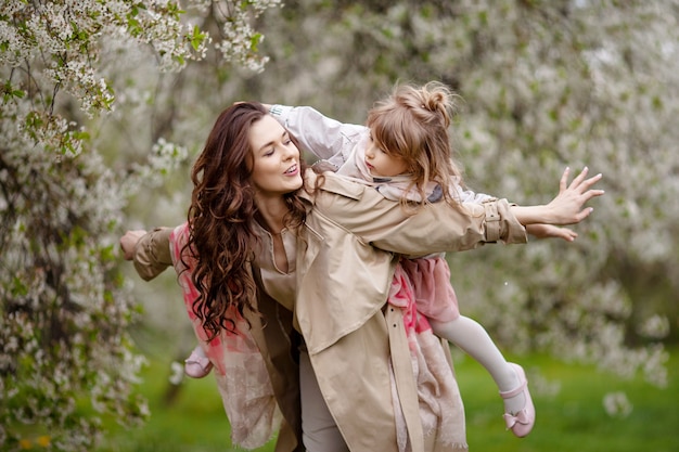 Mère avec enfant fille jouant dans le jardin de printemps fleuri. Femme avec sa fille étreindre et s'amuser à l'extérieur. Concept de famille heureuse