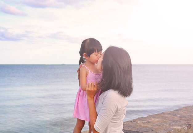 Mère et enfant fille s&#39;embrasser avec émotion naturelle sur fond de mer dans la soirée