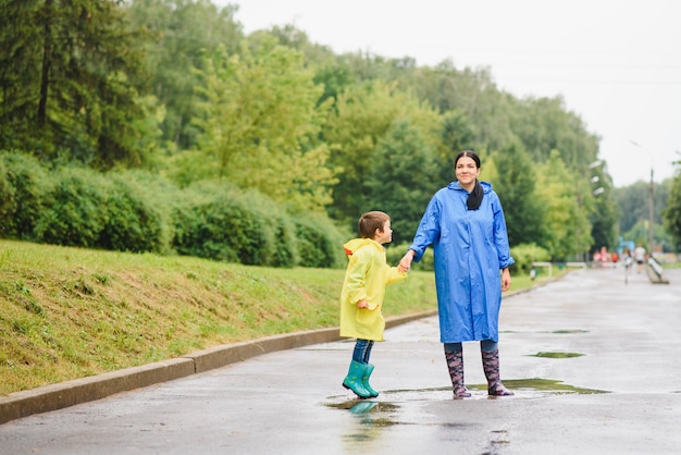 Mère et enfant jouant sous la pluie, portant des bottes et des imperméables