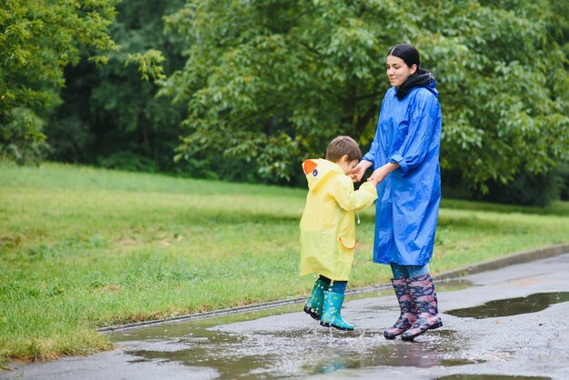 Mère et enfant jouant sous la pluie, portant des bottes et des imperméables