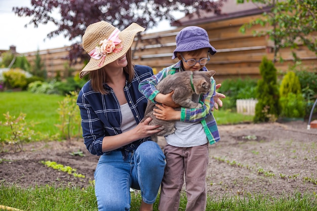 La mère et l'enfant jouent avec le chat domestique dans le jardin d'arrière-cour