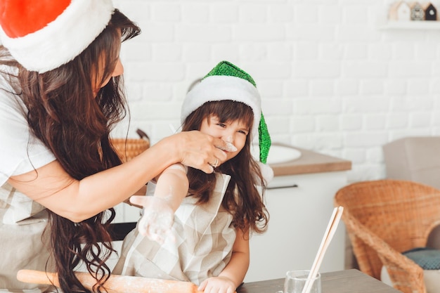 Une mère et un enfant joyeux et joyeux dans les chapeaux du père Noël préparent des biscuits de Noël dans la cuisine du nouvel an et de Noël
