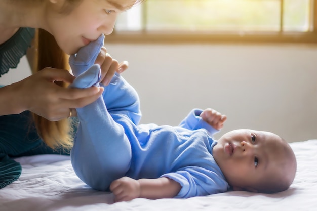 Mère et enfant sur le lit. Maman et bébé garçon jouant dans la chambre ensoleillée.