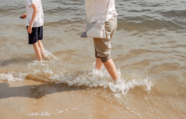 Mère et enfant marchant sur une plage de sable. Eau fraîche dans la mer. Marchez le long de la plage pieds nus. Frais en été dans la chaleur. Petites vagues sous les pieds