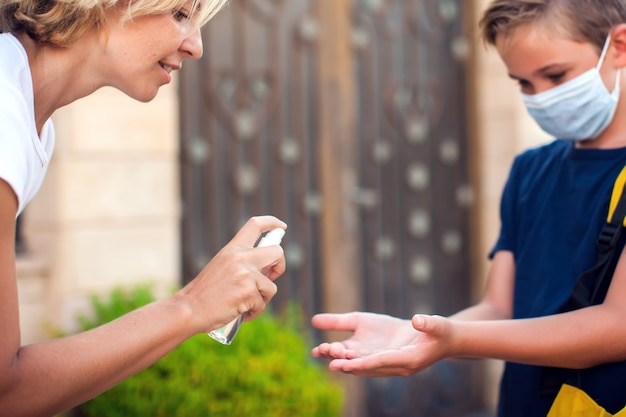 Mère et enfant avec masque médical désinfectant les mains avec un désinfectant à l'extérieur