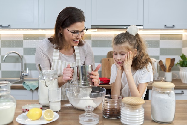Mère et enfant préparant la boulangerie ensemble dans la cuisine à domicile. Une femme tamise la farine, apprend à sa petite fille à cuisiner des cupcakes. Cuisine maison, famille, communication parent-enfant