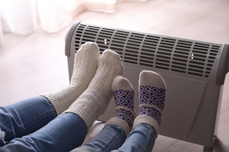 Photo mère et enfant réchauffant les pieds près d'un chauffage électrique à la maison en gros plan