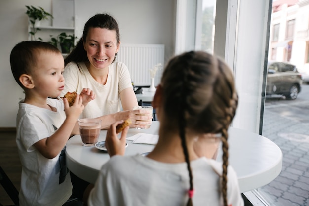 Mère avec enfants buvant du chocolat chaud et du café au lait dans un café local. Ils sourient et s'amusent. Concept de maternité