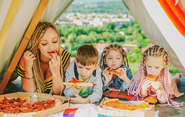 Mère avec enfants jouant ensemble manger de la pizza dans la tente camping familial maman avec enfants s'amusant o