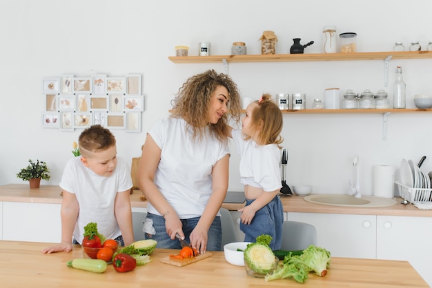 Mère avec enfants préparant une salade de légumes à la maison