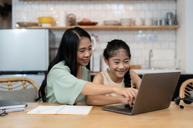 Mère enseignant aux enfants à faire leurs devoirs à la maison Heureuse famille asiatique utilisant l'ordinateur portable ensemble à la maison Jeunes parents de famille asiatiques aidant leur fille à dessiner à la maison