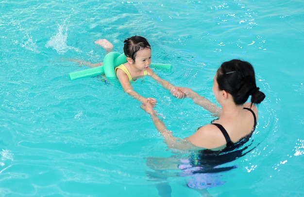 Mère enseignant enfant dans la piscine avec nouille en mousse