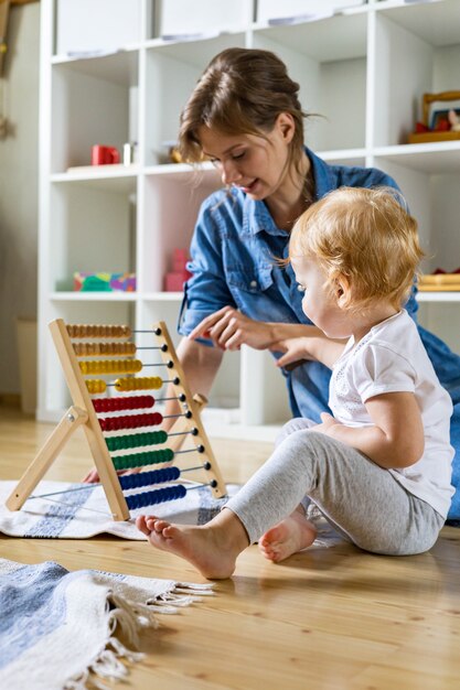 Mère enseignant un petit enfant comptant sur un boulier écologique en bois enfantin multicolore sur le sol