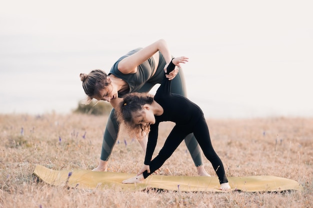 Mère enseigne à la jeune petite fille faisant du yoga à l'extérieur sur fond de mer Mode de vie sain