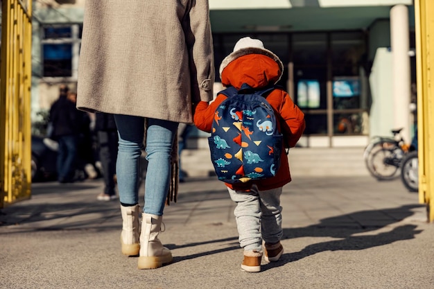 Une mère entrant dans la cour de la maternelle avec son garçon d'âge préscolaire