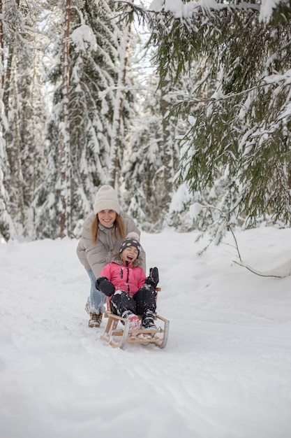 Mère avec équitation sur traîneau et rire dans la forêt d'hiver