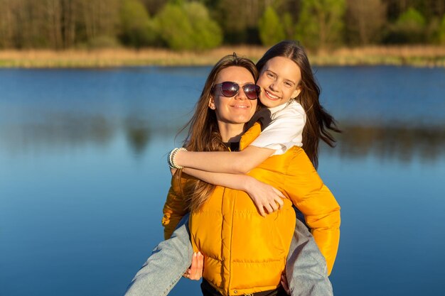 Mère espiègle donnant à sa fille une promenade sur le dos au printemps au bord du lac