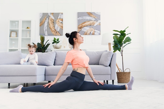 Mère faisant des exercices du matin pendant que sa fille joue à la maison.