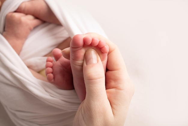 La mère fait un massage sur son pied de bébé. Gros plan des pieds de bébé dans les mains de la mère. Prévention des pieds plats, développement, tonus musculaire, dysplasie. Concepts de famille, d'amour, de soins et de santé. Macro d'atelier.