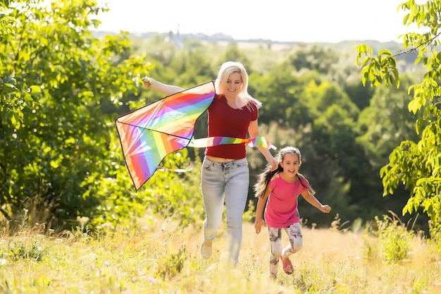 mère de famille heureuse et enfant courent sur le pré avec un cerf-volant en été sur la nature