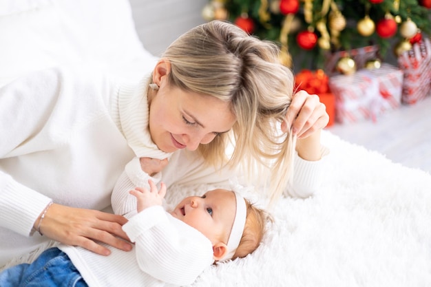 Une mère de famille heureuse et un enfant décorent un arbre de Noël bébé avec sa famille à la maison pour les vacances de Noël Un bébé avec sa mère dans une pièce décorée de façon festive avec un arbre de Noël