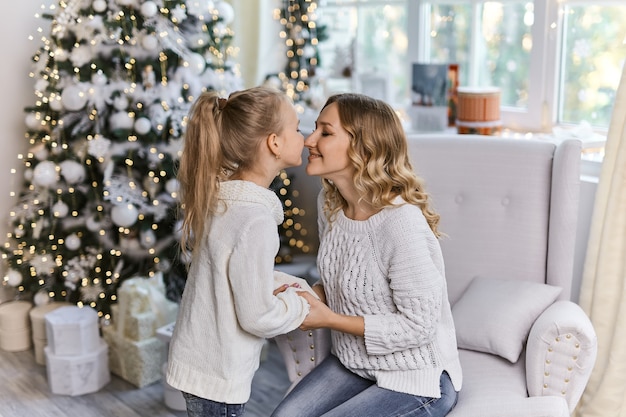 Mère de famille heureuse et fille d'enfant le matin de Noël à l'arbre de Noël avec des cadeaux