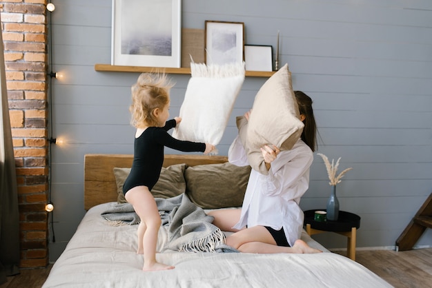 Mère et fille actives tenant des oreillers se battant sur le lit