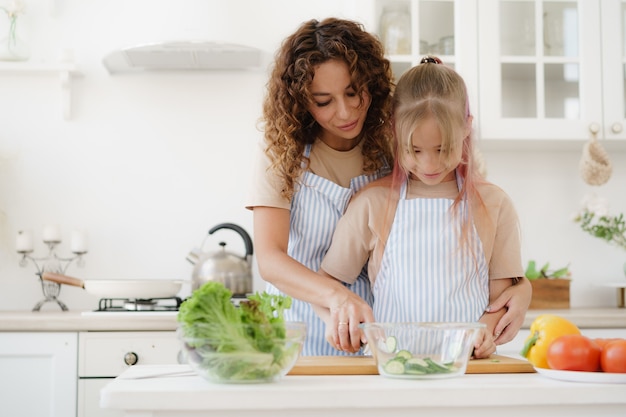 Mère et fille de l'adolescence préparant une salade de légumes à la cuisine