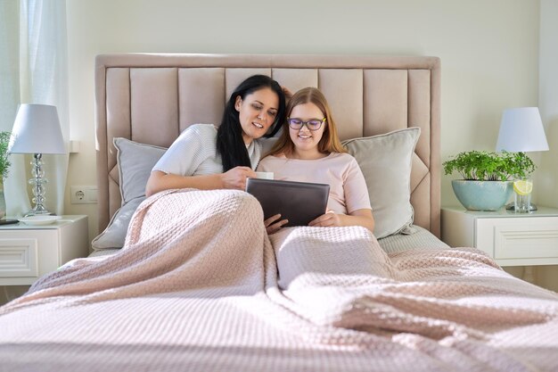 Mère et fille adolescente se reposent ensemble à la maison en utilisant une tablette numérique