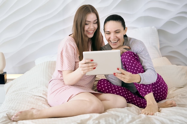 Une mère avec une fille adulte regarde une vidéo amusante sur l'écran d'une tablette tout en étant assise dans son lit