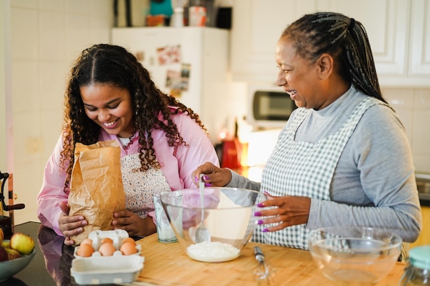 Mère et fille africaines préparant un gâteau aux fruits à la maison Focus sur les mains des filles tenant le sac