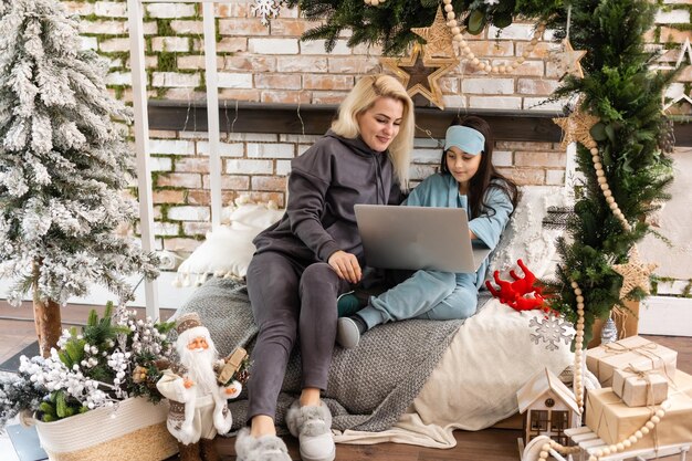 mère et fille à l'aide d'un ordinateur portable Appel vidéo Facetime Chat Communication au père avec la décoration de l'arbre de Noël dans la salle blanche à la maison. Visage souriant et heureux de célébrer le nouvel an festif.