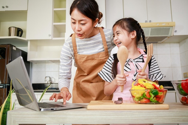 Mère et fille asiatiques préparant une salade et utilisant une méthode en ligne à partir d'un ordinateur portable