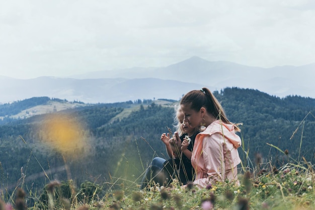 Mère et fille assise sur une colline avec vue sur la montagne derrière. Bonne famille voyageant et vacances