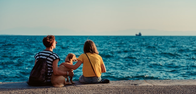 Mère et fille assise sur le front de mer avec chien