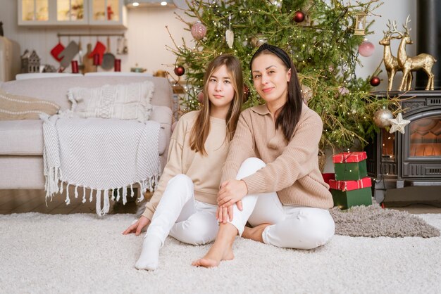 Mère et fille assises sur le sol avec un arbre de Noël en arrière-plan