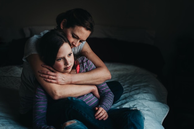 Mère et fille attentionnées assises sur le lit à la maison