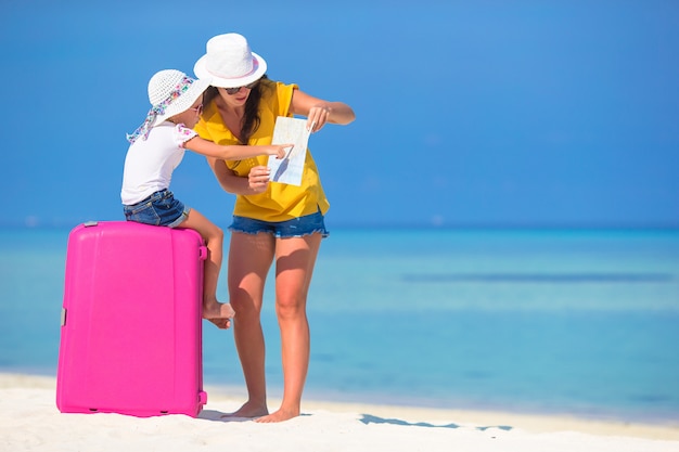 Mère et fille avec bagages et carte sur la plage